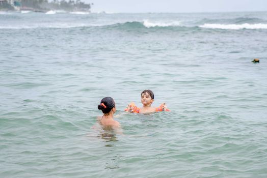 A mother and her child swim in the ocean, enjoying a relaxing day at the beach.