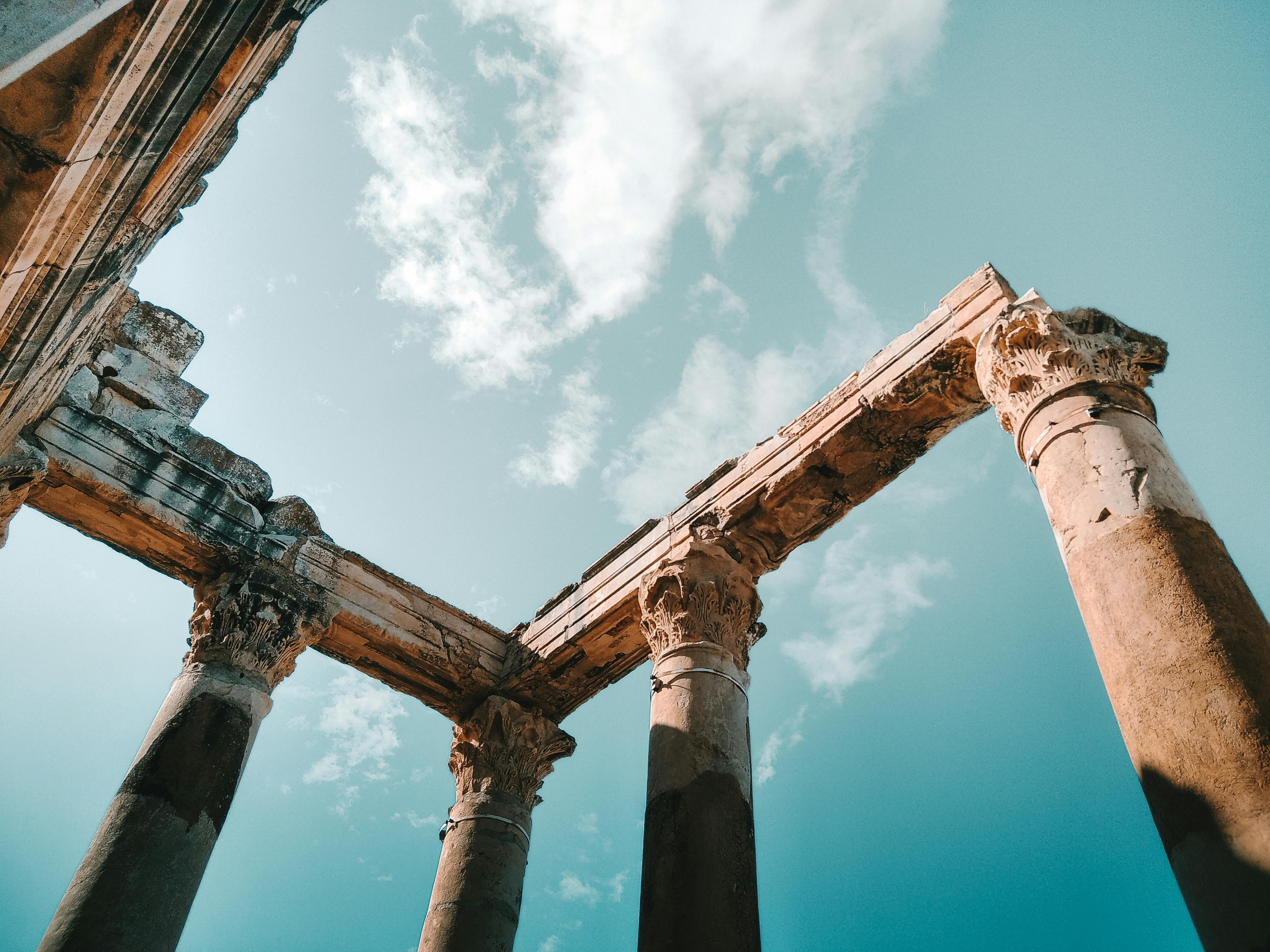 Captivating low-angle shot of ancient pillars and arches set against a vibrant blue sky with clouds.