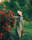 Woman in a Straw Hat and Green Dress by Bush Full of Red Roses