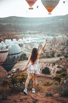 A woman with a floral dress and brown hair releases a smoke bomb amidst hot air balloons in Turkey.