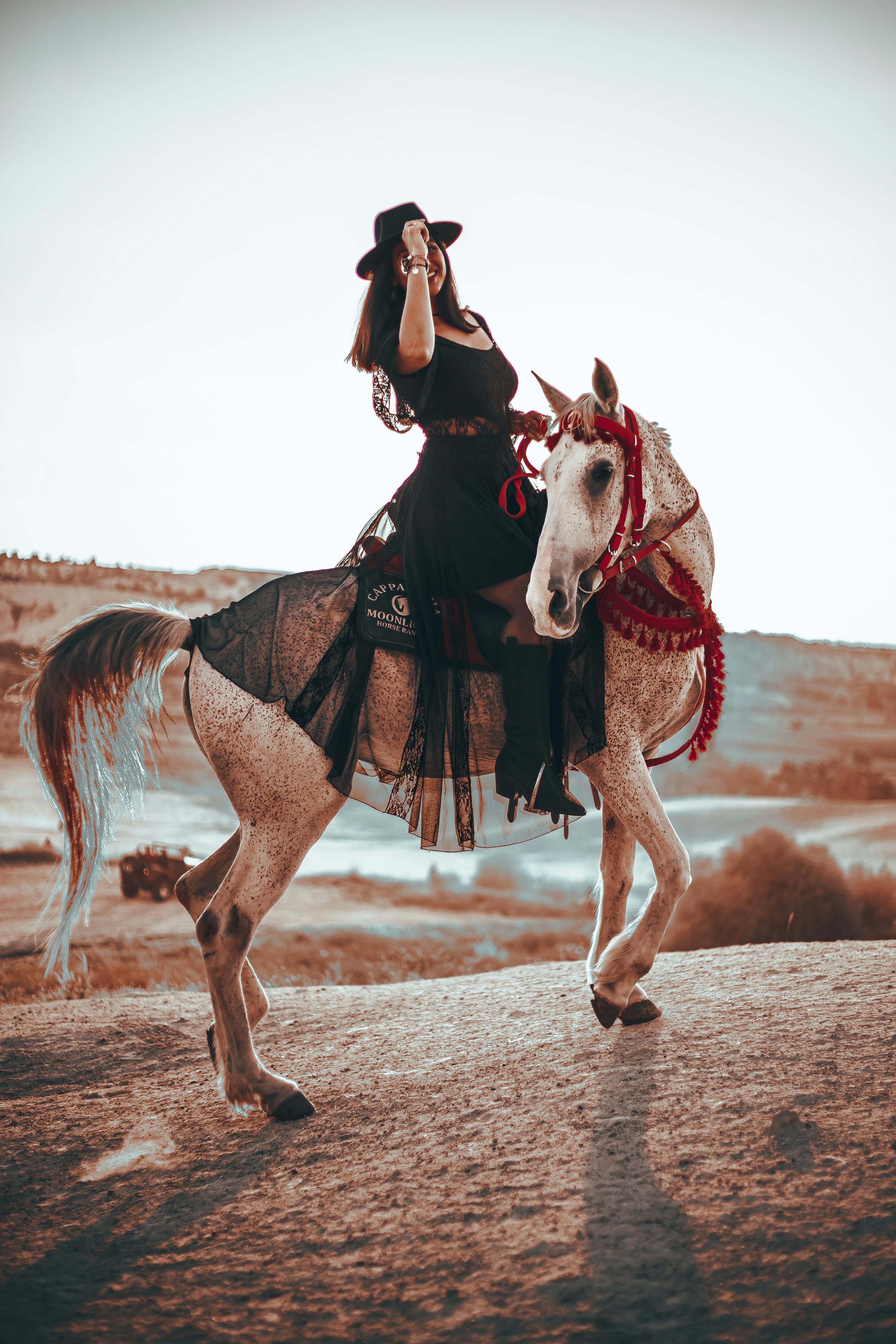 woman in a black hat on a white horse with red bridle