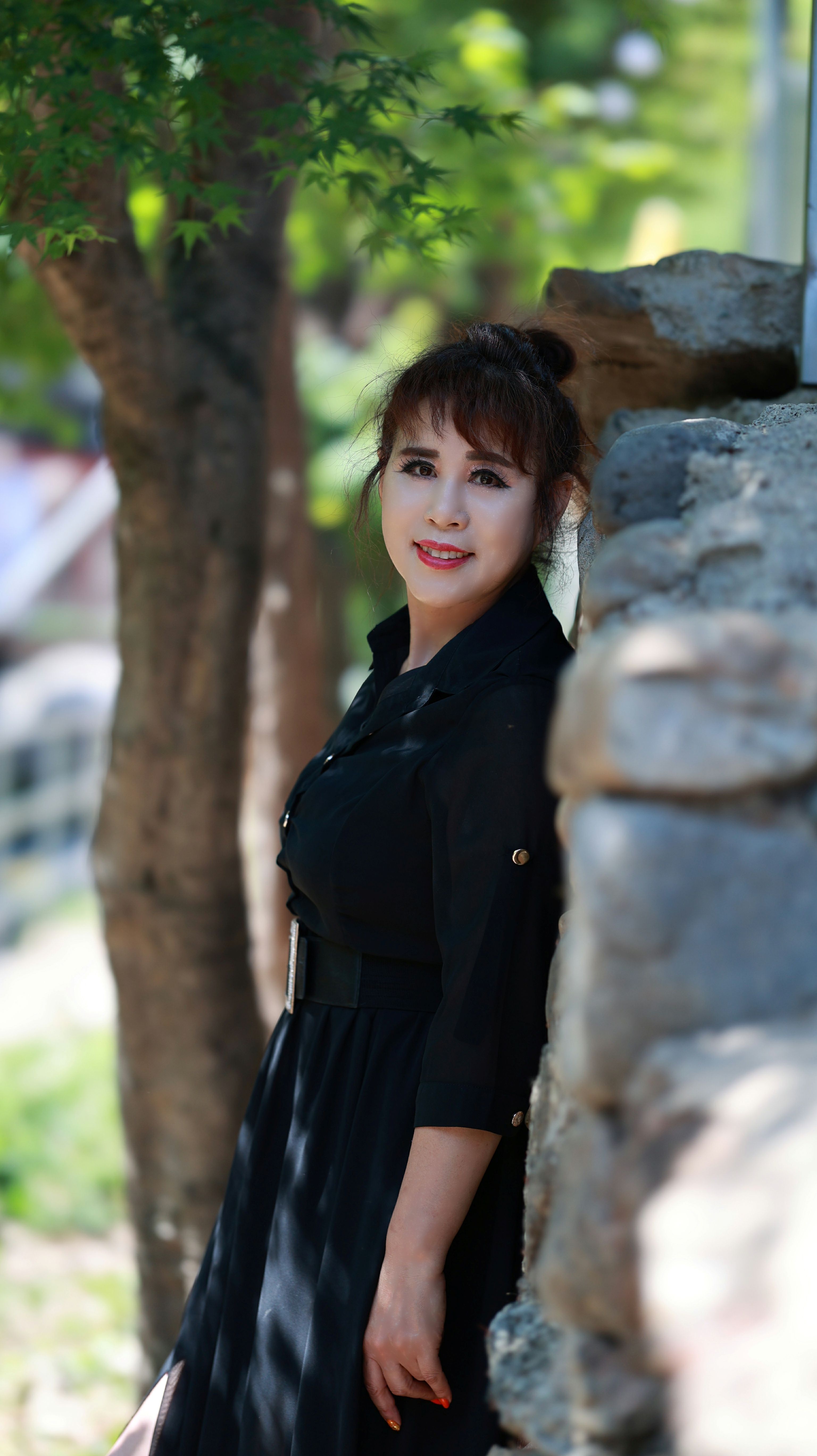 Stylish woman standing by a stone wall in a sunny outdoor setting, exuding confidence.