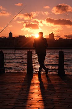 Silhouette of a person against a vibrant sunrise at a riverside, casting long shadows.
