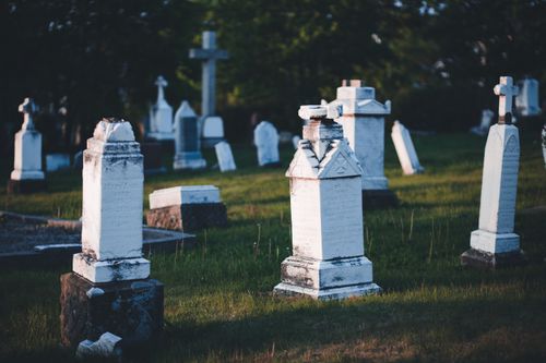 Free A peaceful cemetery scene with aged tombstones and crosses, captured at sunset with lush greenery. Stock Photo