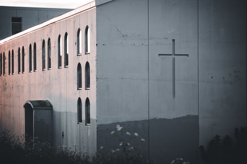 Free A minimalist church facade featuring arched windows and a prominent cross in neutral tones. Stock Photo