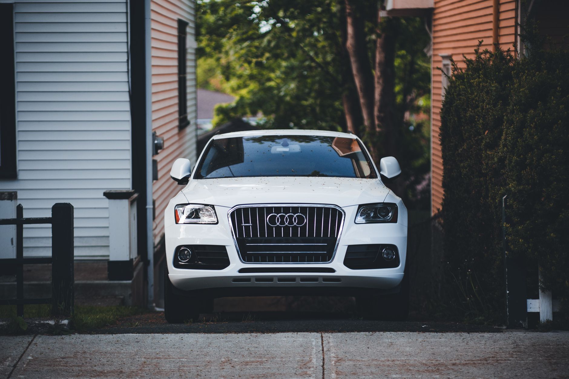 White Audi car parked outdoors between two houses on a sunny day, showcasing elegance and design.