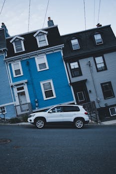 Colorful houses on a slope with a white car parked on the street, showcasing urban charm.