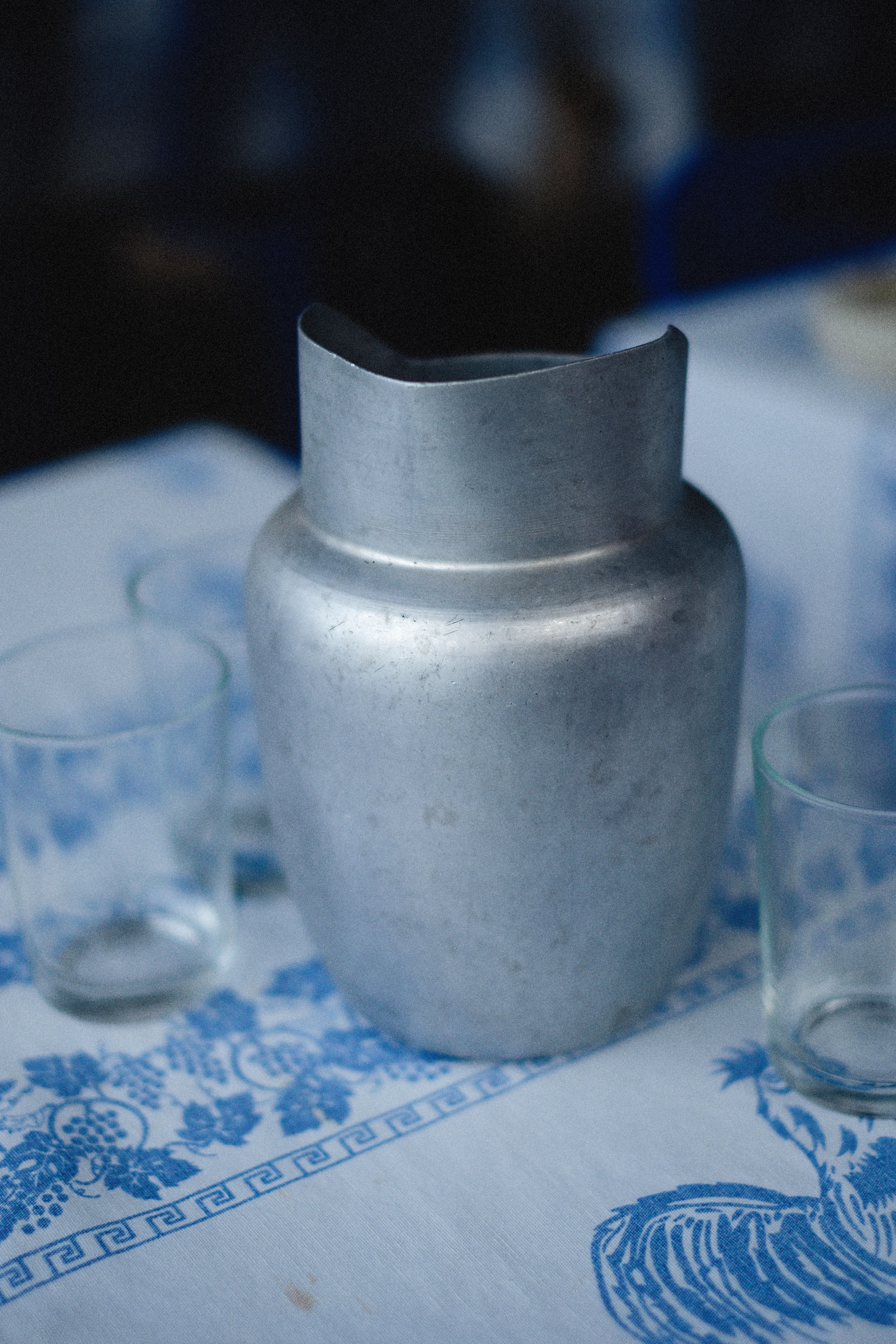 Close-up of a vintage metal pitcher on a blue-patterned tablecloth, evoking nostalgic charm.