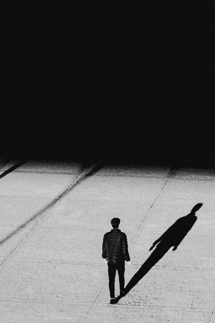 Black and white photo of a man with a long shadow on a concrete surface, emphasizing solitude.