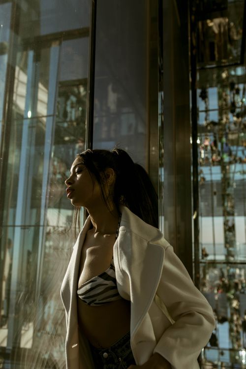 Free Elegant portrait of a stylish woman in a white coat by a reflective modern building in New York City. Stock Photo