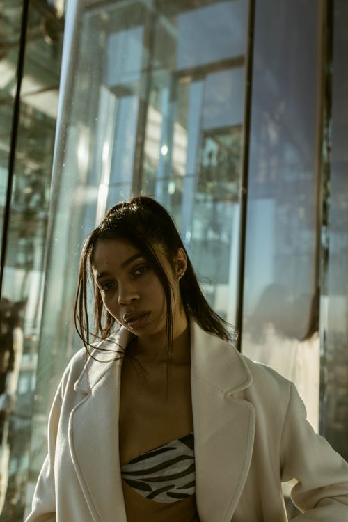Free Young woman posing confidently against modern glass architecture at sunset. Stock Photo