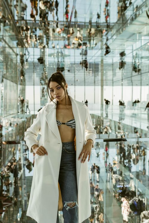 Free Woman in designer coat poses amidst modern mirrored architecture in New York City. Stock Photo