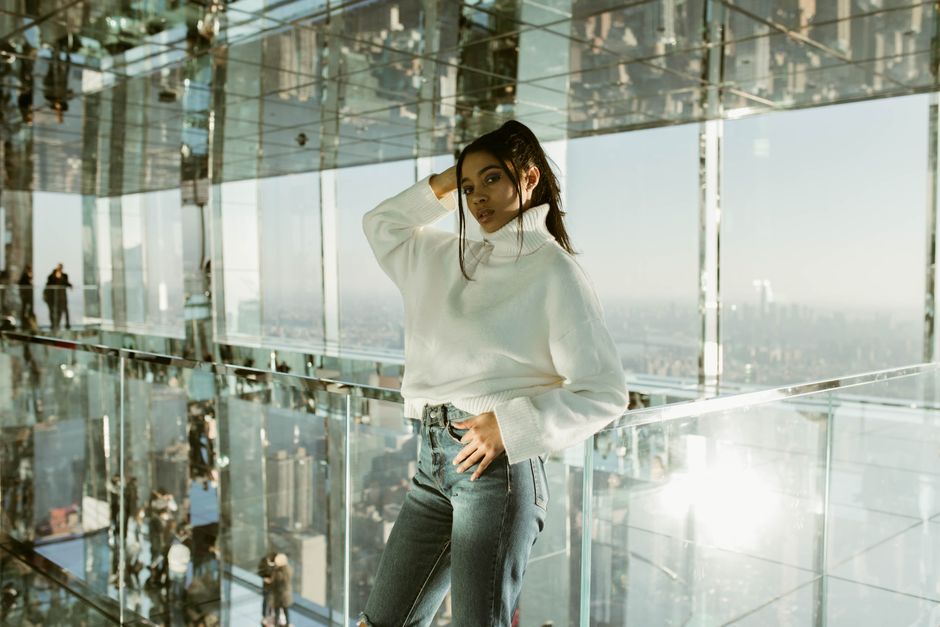 Fashionable woman posing in mirrored interior with cityscape view.