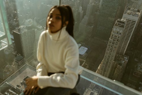 Free Woman in White Sweater Sitting on a Glass Window Stock Photo
