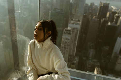 Free A serene portrait of a woman in a white sweater atop a New York skyscraper with city skyline. Stock Photo