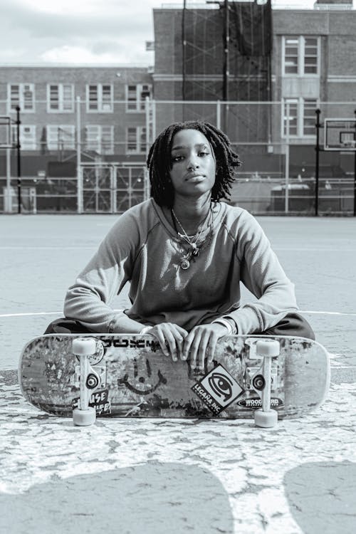 Woman Sitting on the Ground while Holding Her Skateboard