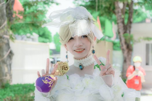 A smiling cosplayer in an ornate costume poses outdoors showing peace signs, exuding joy and creativity.