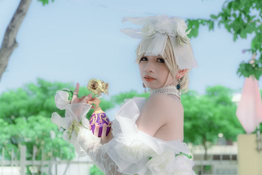 Cosplayer in elegant white costume posing with flower outdoors.
