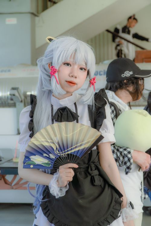 Free Anime cosplayer in maid outfit with fan, posing indoors. Vibrant and playful scene with costume details. Stock Photo