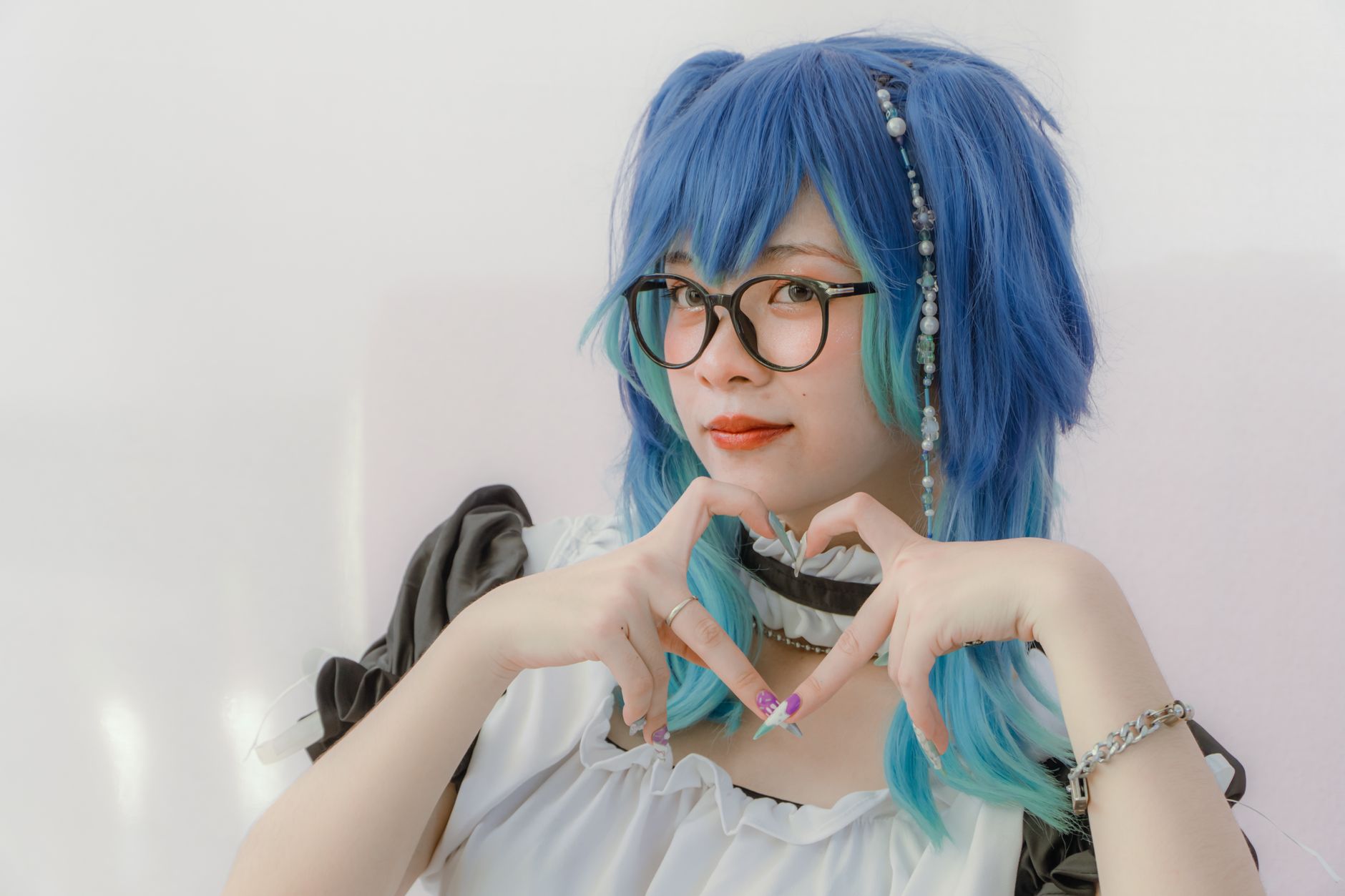 Creative cosplay portrait featuring a woman in costume with blue hair and glasses, forming a heart gesture.