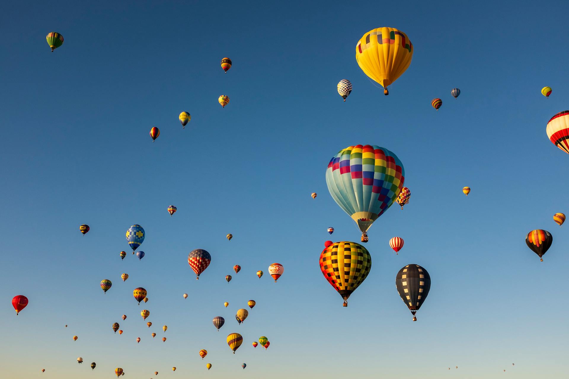 Vivid hot air balloons float in a clear blue sky during a New Mexico festival.