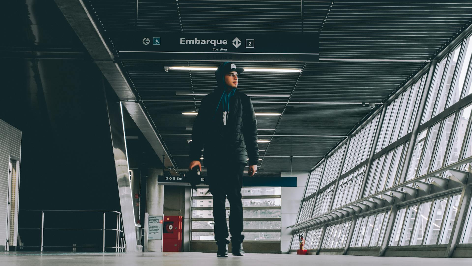 A man stands in a modern terminal with large windows and overhead signs.