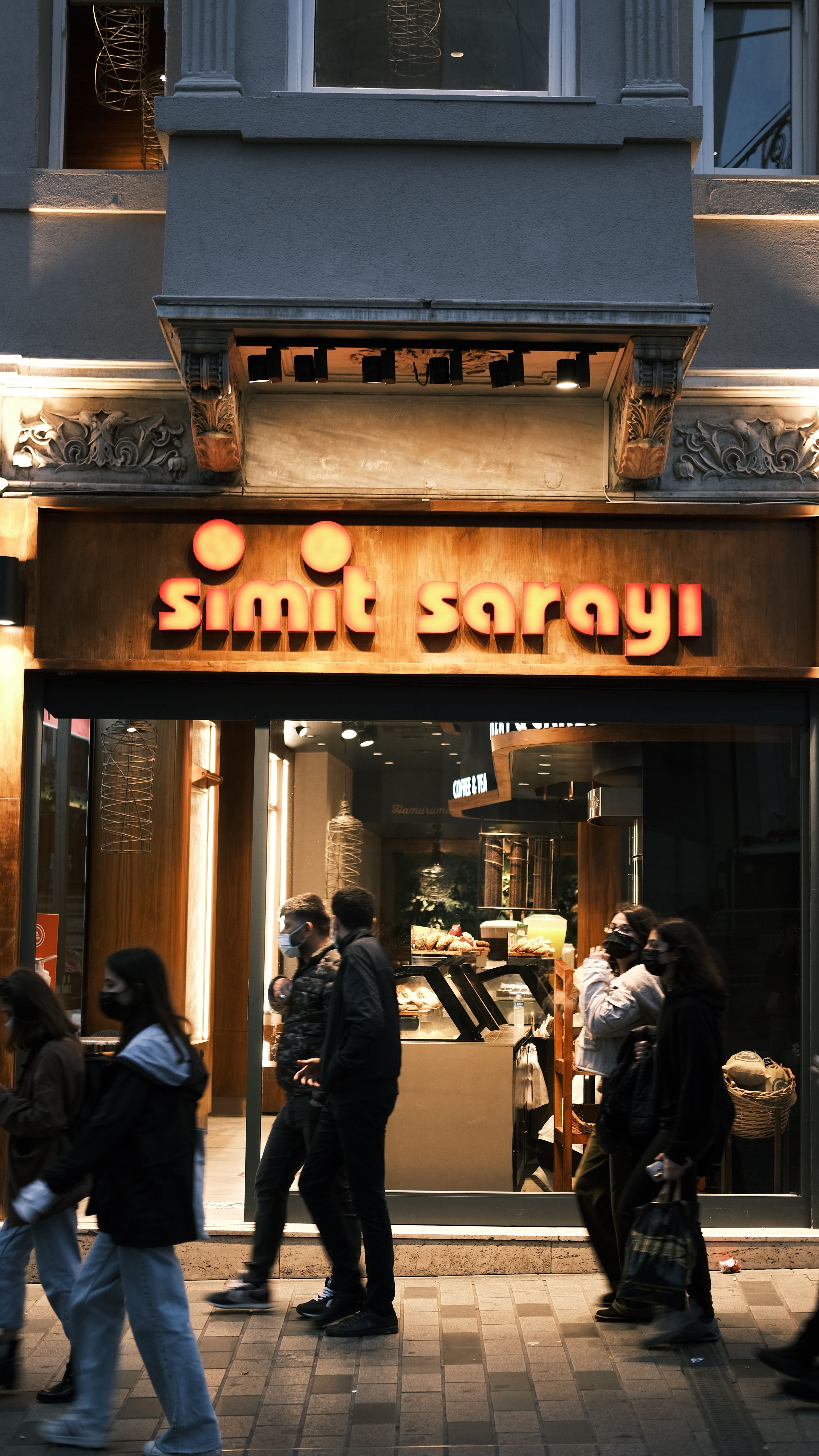 People walk past an illuminated Simit Sarayı shop in Istanbul at night.