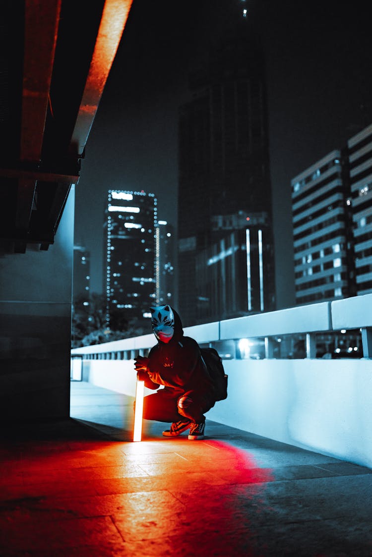 Man In A Blue Mask Crouching On A Balcony At Night