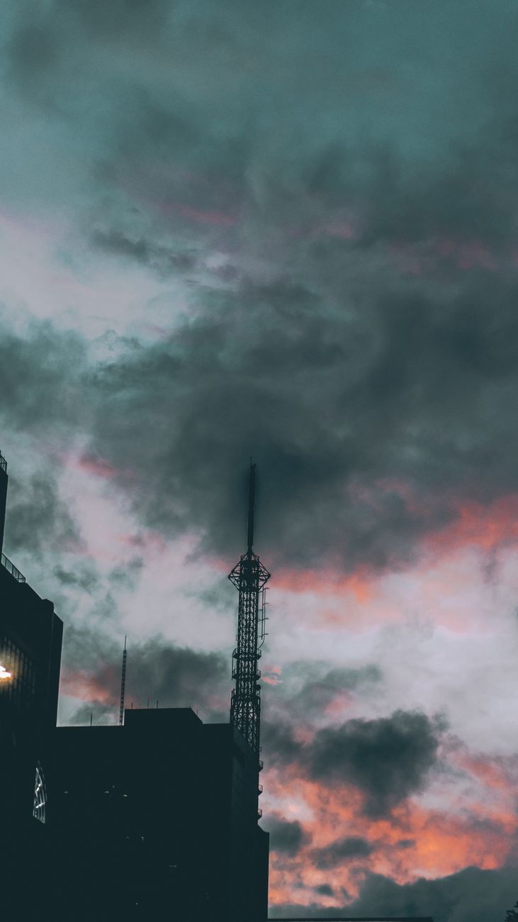 Silhouetted tower against a vivid sunset sky with dramatic clouds in an urban setting.