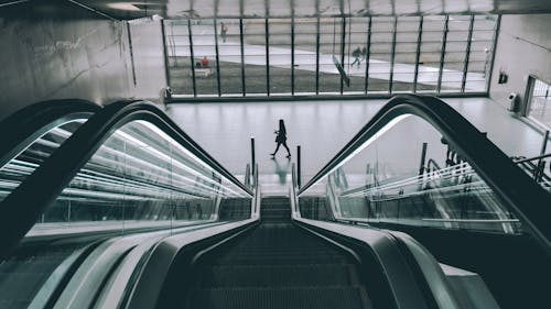 Grayscale Photography of Person Walking Near Escalator