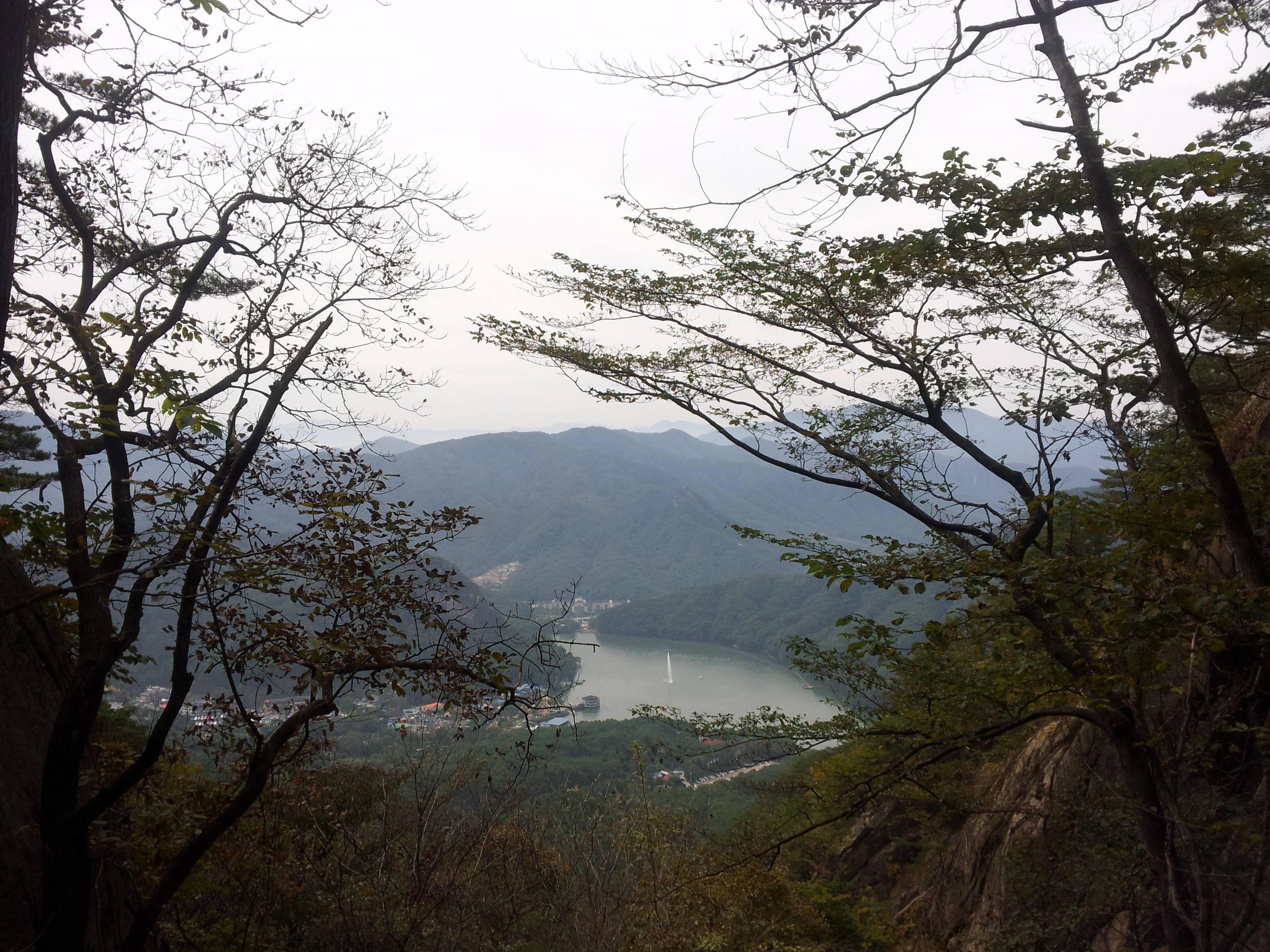 Serene landscape of a lake nestled among mountains in Pocheon, South Korea, framed by trees.