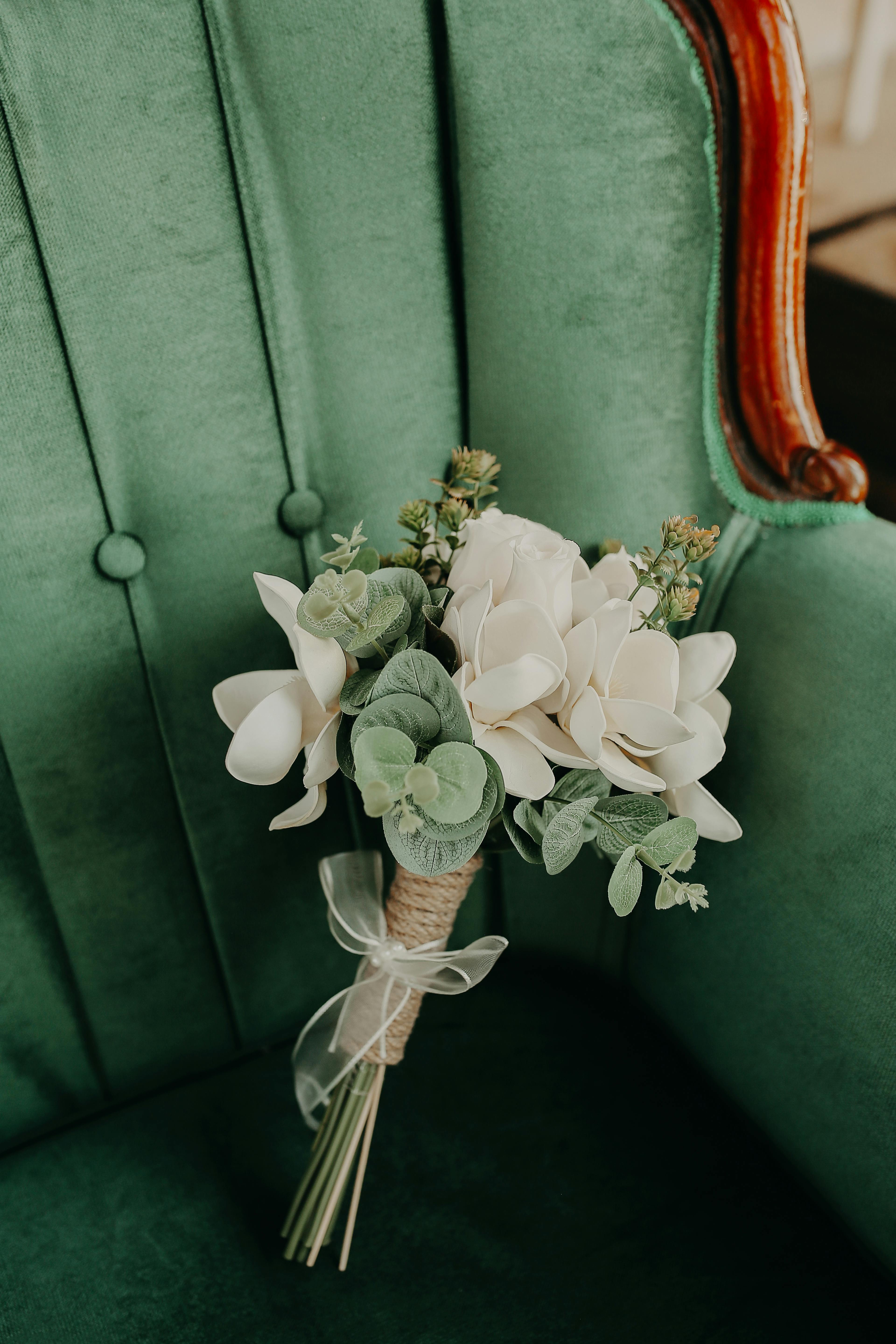 A close-up view of a beautiful white flower bouquet resting on a vintage green armchair.