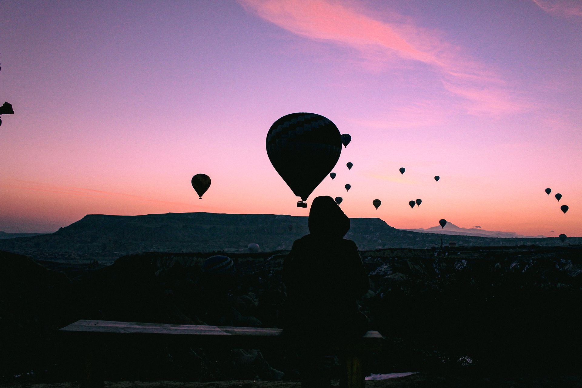 Travellers watching hot air balloons rise over a valley at sunrise — photo by Zeynep yilmaz on Pexels