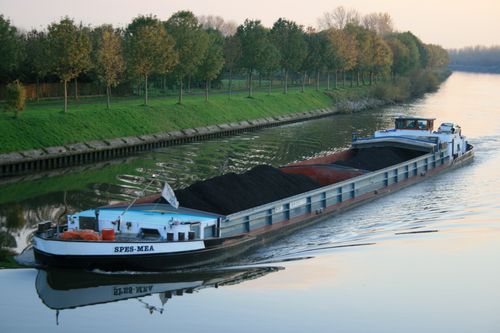 Free Large cargo barge carrying coal along a tranquil canal lined with lush trees during sunset. Stock Photo