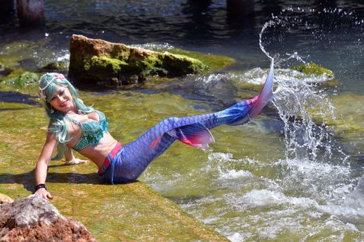 Colorful mermaid costume model splashing water in Garda, Italy.