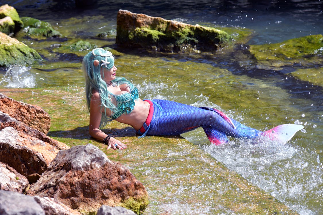 Free Woman in Blue and White Bikini Lying on Brown Rock on Water Stock Photo