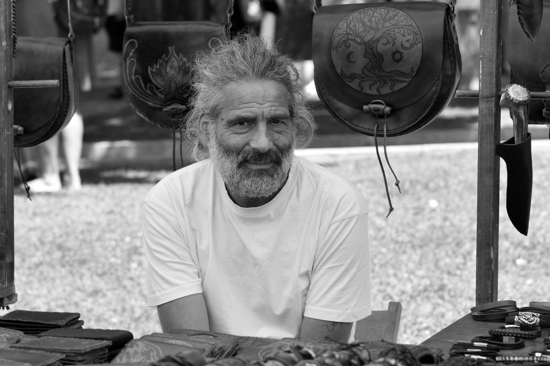 Portrait of an artisan vendor at an outdoor market in Italy, showcasing handmade leather crafts.