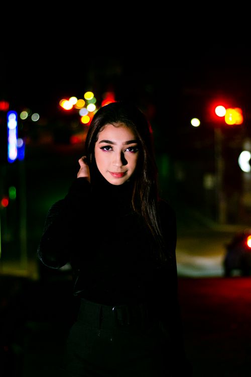 Free Portrait of a young woman in black clothing with vibrant bokeh lights in a nighttime city setting. Stock Photo