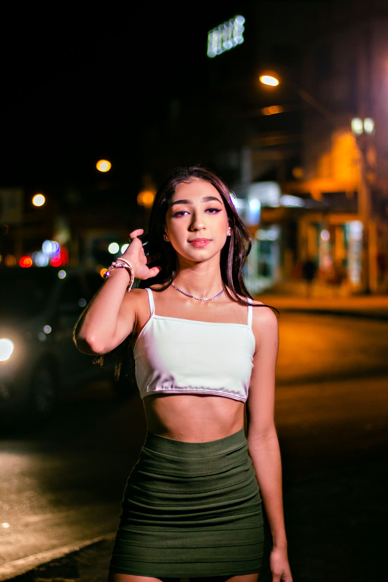 Woman in a white crop top and olive mini skirt at night