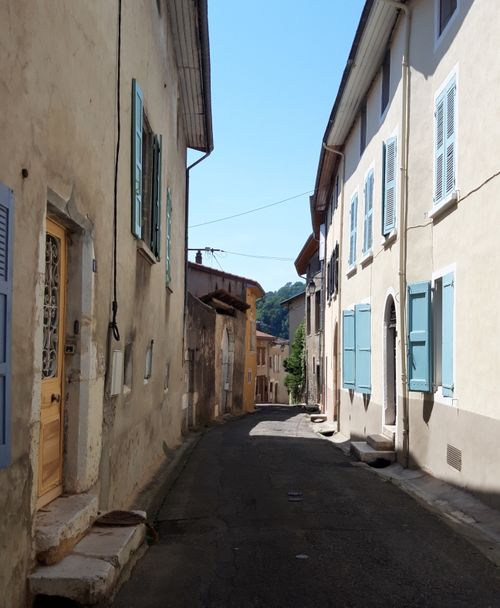 Free A picturesque narrow alley in a Mediterranean village with pastel buildings and blue shutters. Stock Photo