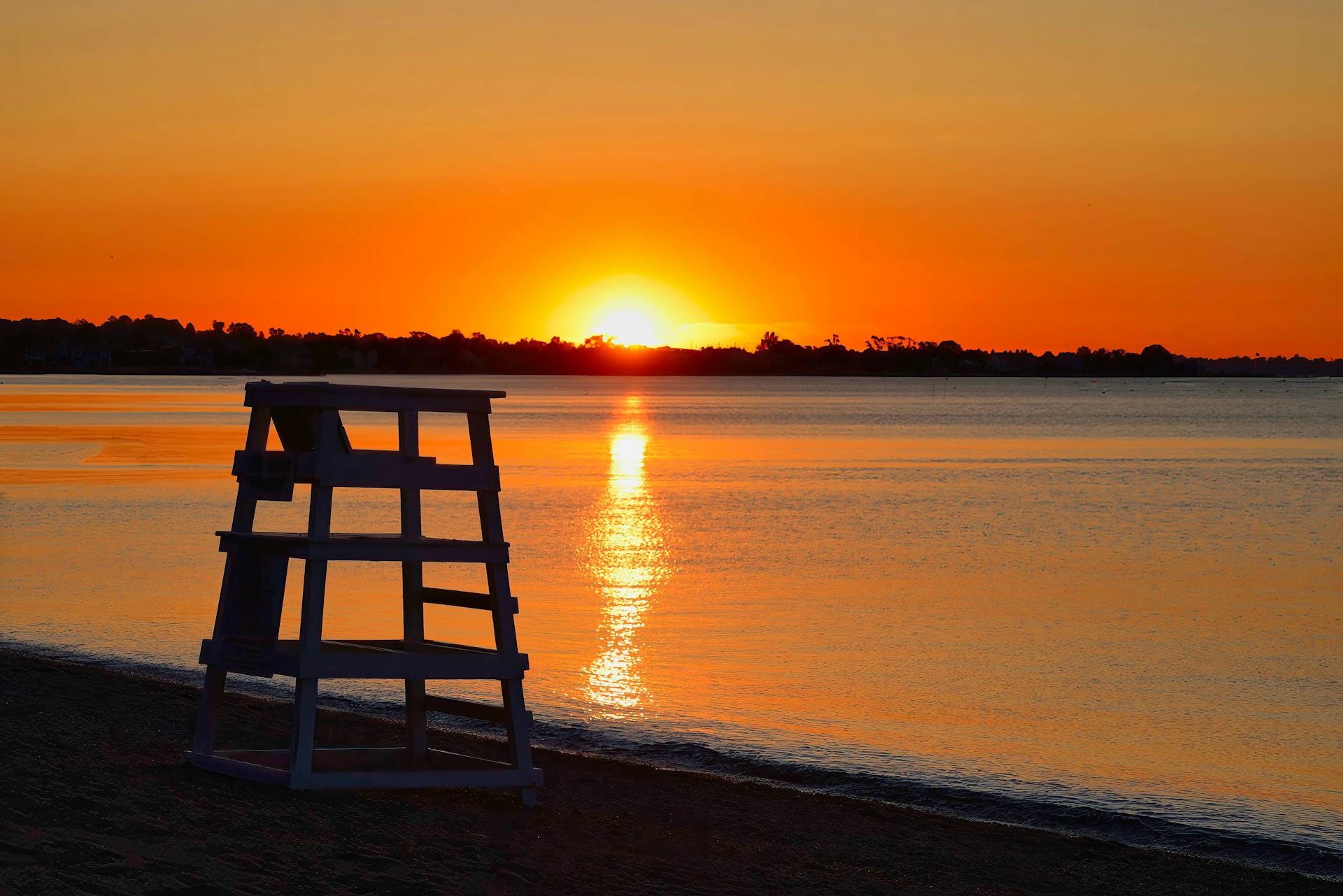 A peaceful sunrise over Norwalk beach, capturing the silhouette of a lifeguard post and calm waters.