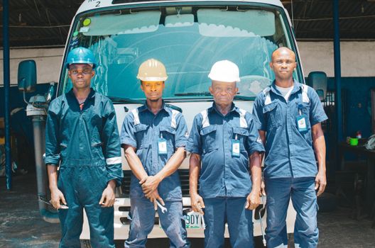 Group of mechanics in uniforms and hard hats in an automotive garage in Nigeria.