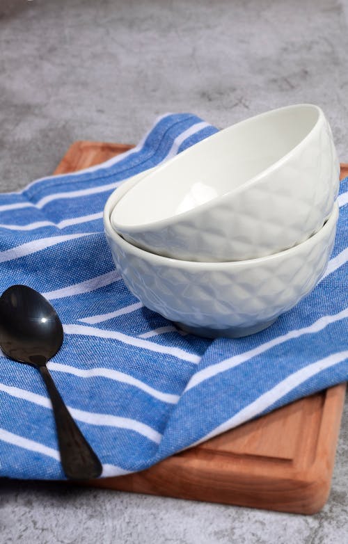 Stacked Ceramic Bowl beside a Spoon on a Wooden Tray with Blue and White Textile 