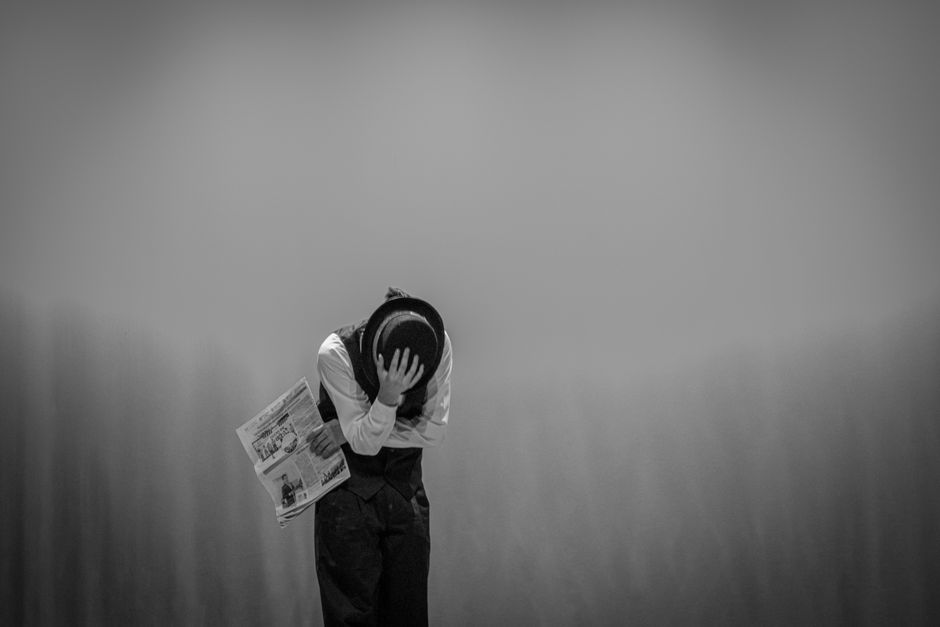A black-and-white image of an adult holding a newspaper, depicting themes of loneliness and sadness.