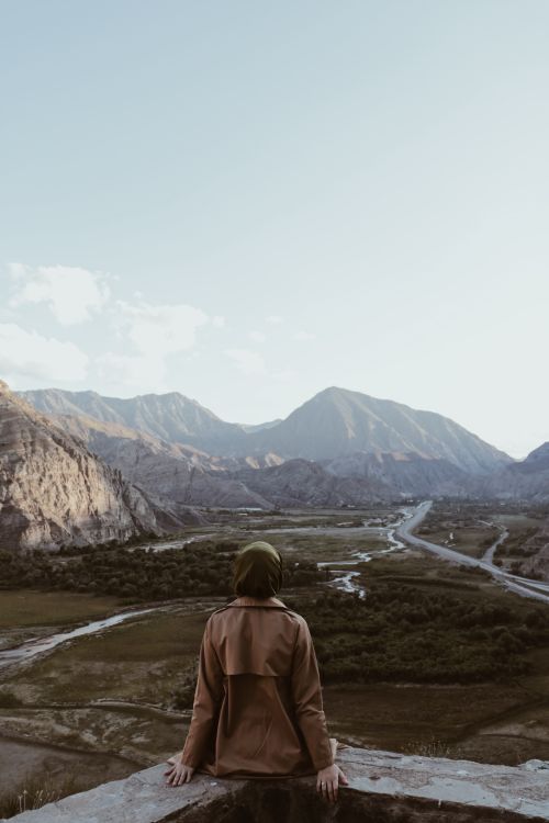 Free Woman sitting in a hijab, overlooking expansive mountain valley in Uzundere, Erzurum, Turkey. Stock Photo