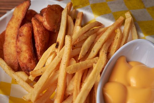 Free Crispy French fries and potato wedges served with cheesy sauce on a checkered tablecloth. Stock Photo