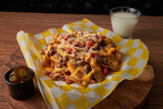 Delicious cheesy nachos topped with jalapenos served on a wooden platter with a drink.