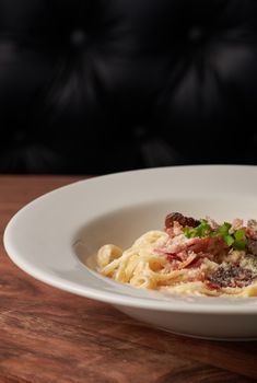 Close-up of creamy Italian spaghetti carbonara with bacon and cheese in a white plate.