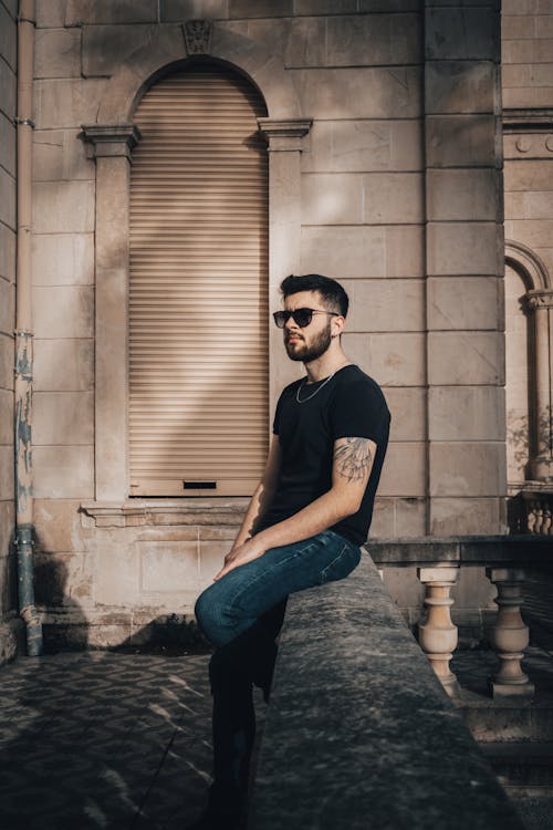 A Bearded Man in Sunglasses Sitting on the Concrete Balustrade