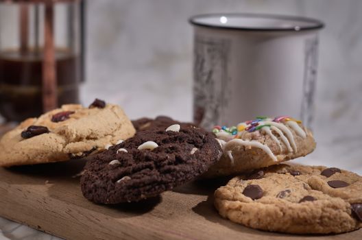 A close-up of various delicious cookies on a wooden board with a coffee cup in the background.
